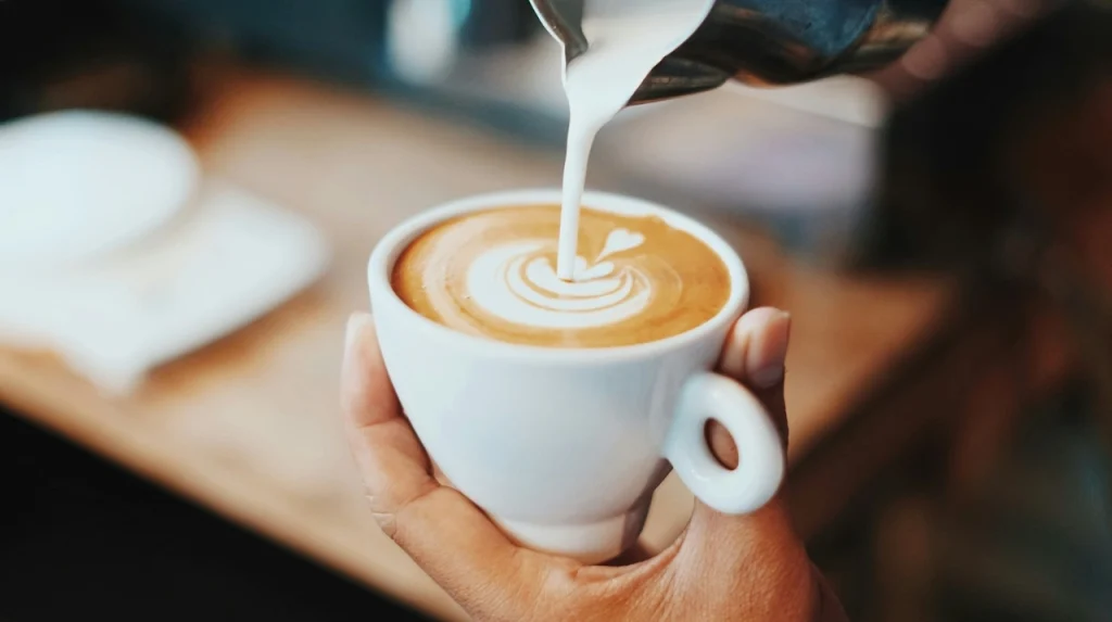 Kahvipäivä Barista kaataa maitoa kahviin ja tekee latte art -kuvion