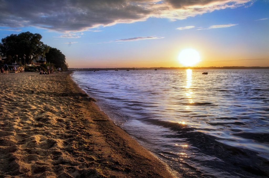 Zachód słońca nad jeziorem i piaszczysta plaża jako pomysł na letni wypoczynek w Polsce.