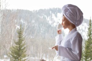 Poranek w dzień singla – kobieta z kubkiem kawy podziwia zaśnieżony krajobraz za oknem.