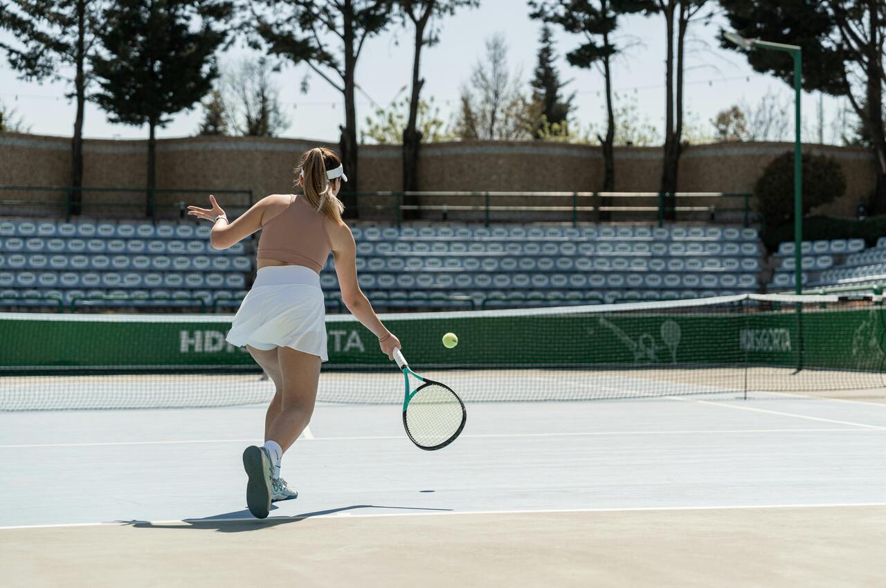 tenis - zasady gry i ciekawostki, kobieta na korcie tenisowym, odbija piłkę przez siatkę, kort twardy 