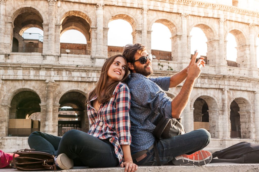 Para turystów odpoczywa przed Koloseum w Rzymie, robiąc wspólne selfie podczas city breaku we Włoszech.