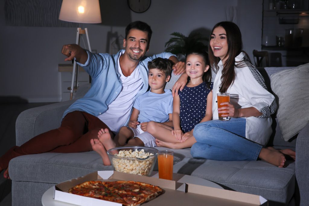Rodzina z dziećmi spędzająca wspólny wieczór na kanapie, oglądanie filmu, pizza i popcorn jako sposób na świętowanie Dnia Rodziny 15 maja.