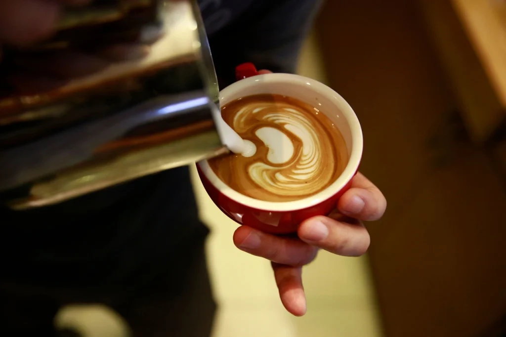 Barista nalewający spienione mleko do filiżanki kawy i tworzący latte art – Dzień Kawy.