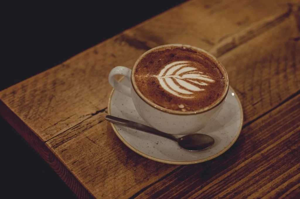 Filiżanka cappuccino z latte art na drewnianym stoliku – Międzynarodowy Dzień Kawy.