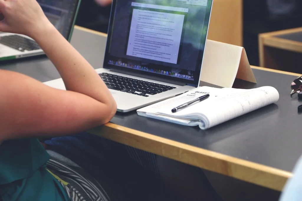 Osoba ucząca się przy laptopie i notatkach, dla której prezent na zakończenie studiów może być miłym zwieńczeniem akademickiej drogi.