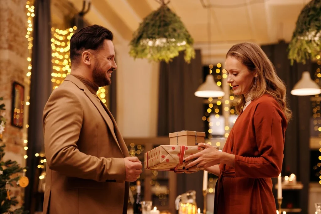 Uśmiechnięty mężczyzna wręcza żonie elegancko zapakowany upominek podczas romantycznego wieczoru - wyjątkowy prezent dla żony na specjalną okazję.